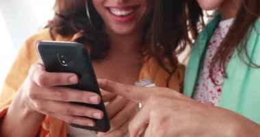 Girls using smartphone looking at screen together. Casual women laughing and smiling