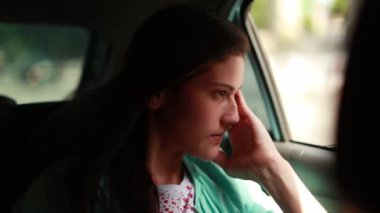 Arabanın arka koltuğundaki düşünceli genç kadın duygularını değiştiriyor. Düşünceli kız, farklı ruh halleri, pencereden dışarı bakıyor.