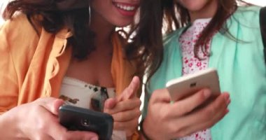 İki kız ellerinde akıllı telefon cihazları, gülüyorlar ve internetten gülümsüyorlar.