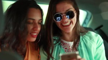 Milenyum kızları arabanın arkasında akıllı telefon aygıtı ekranına bakıyor.