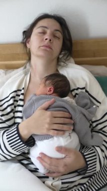 Öğleden Sonra Kestirme Sahnesi - Yorgun Anne ve Yenidoğan Bebek 'in İlk Günleri sırasında Yatakta Birlikte Uyuyor, dikey video. Bebek göğsünde tutuluyor.
