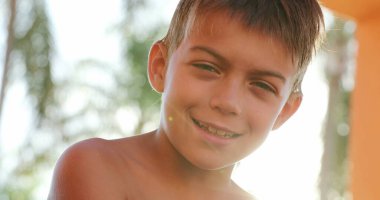 Child looking to camera smiling portrait of young boy outside with lens-flare sunlight