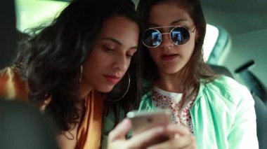 İki genç milenyum kızı arabanın arka koltuğunda akıllı telefona bakıp gülüyor.