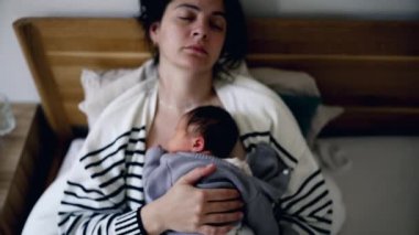 Uyuyan anne, yeni doğmuş bebeği yatakta huzur içinde kucağında bebekle uyuyor. Yaşamın ilk günlerinde uyukluyor, otantik anne bakımı sahnesi.
