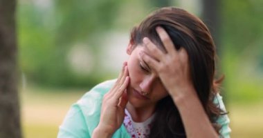 Pensive young woman feeling regret at park. Concerned girl