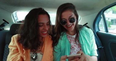 Girlfriends in backseat of car using smartphone. Millennial women using taxi and cellphone