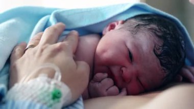 Yeni doğmuş bebek doğduktan hemen sonra annesinin göğsünde dinleniyor. Battaniyeyle örtülmüş. Bebek ilk kez dünyayı keşfediyor.