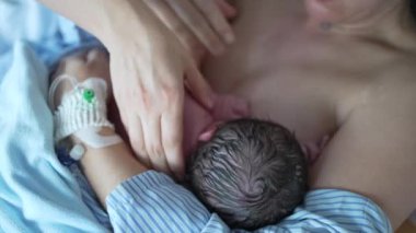 Yeni doğan bebek doğumdan hemen sonra ilk kez emziriliyor. Deriyle teması vurguluyor. Hemşirenin eli, bebeğe bakması için yeni anneye yardım ediyor.