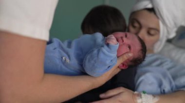 Anne ve çocuğu, doğumdan sonra kucağında bebeğiyle hastaneye geliyor. Hemşire küçük bebeği klinikte annesinin yanında kardeşinin koluna veriyor. Kardeşler ilk kez kaynaşıyor.