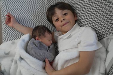 Genç bir çocuk ve yeni doğan kardeşi birbirlerine sarılıp, sevgi ve sıcaklık saçarak barışçıl bir aile ortamında paylaştıkları özel bağı sergiliyorlar..