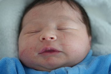 Huzurlu bir yakın plan bebek yüzü, huzur içinde uyuyor, bir bebeğin ilk günlerindeki narin özelliklerini ve sakinliğini vurguluyor.