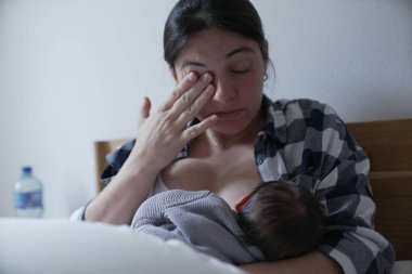 Bir anne bebeğini emzirirken gözyaşlarını siler, erken anneliğin duygusal ve hassas yönlerini yansıtır..