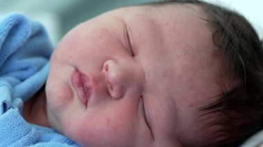 Huzur içinde uyuyan yeni doğmuş bir bebeğin huzur dolu bir anında yeni hayatın narin özelliklerini ve saf masumiyetini yakalıyor.