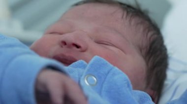 Mavi tulumlu yeni doğmuş bir bebeğin gözleri kapalı bir şekilde huzurlu bir şekilde uyuması. Yumuşak cilt ve gevşek ifade, çocukluk döneminin huzurlu ve hassas anlarını vurgular.