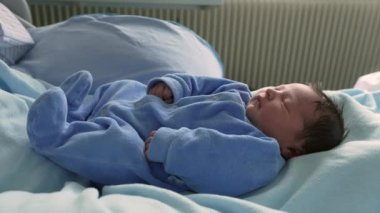 Tatlı yeni doğmuş bebek mavi bir elbisenin içinde mışıl mışıl uyuyor, yumuşak battaniyelere sarılmış, erken çocukluk anlarının sıcaklığını ve huzurunu yakalıyor, yeni doğan bakımını ve aile hayatını.