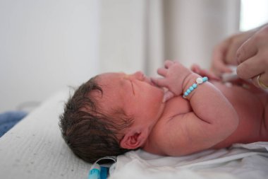 Yeni doğan bebek banyodan sonra giyiniyor, üstünü değiştiriyor, isim bileziği takıyor, yakın plan çekimi erken bakım rutinlerini vurguluyor, anne şefkati ve bakım evindeki hassas anlar.