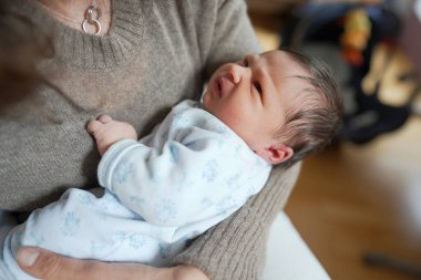 Yeni doğmuş bebek bir yetişkinin kollarında dinleniyor, merakla yukarıya bakıyor, huzurlu bir bağ kurma anını yakalıyor ve dünyayı sıcak ve şefkatli bir şekilde keşfetmenin ilk aşamalarını yakalıyor.