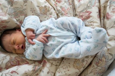 Mavi desenli bebek tulumuyla çiçek desenli bir battaniyenin üzerinde huzur içinde dinleniyor, rahat ve rahat bir ortamda erken yaşamın huzurlu ve narin anlarını sergiliyor.