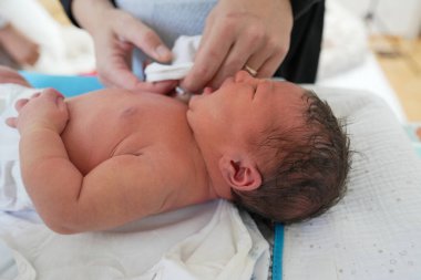 Yeni doğan bebek değişen bir paspasın üzerinde yatarken, bir yetişkin nazikçe bebeği temizler ve onunla ilgilenir, erken yaşlarda, yumuşak ve sakin bir ortamda, gerekli olan hassas ve hassas bakımı vurgular.