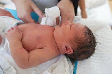 Yeni doğmuş bir bebeğin, bir yetişkin tarafından nazikçe temizlenmesi, bebeğin huzurlu yüz ifadesini ve bakıcı tarafından gösterilen dikkati vurguluyor, şefkat ve erken bağ kurmaya odaklanıyor.