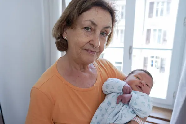 Stock image Proud grandmother holding her newborn grandchild wrapped in a cozy blanket, both looking content and connected, capturing a moment of familial love and the special bond between grandparent and grandchild