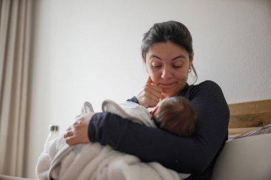 Anne bebeğini kucağında tutarken emziriyor. Yorgunluk ve şefkat karışımı bir şey taşıyor. Ebeveyn yolculuğunun doğasında olan bağlılığın ve sevginin altını çiziyorum.