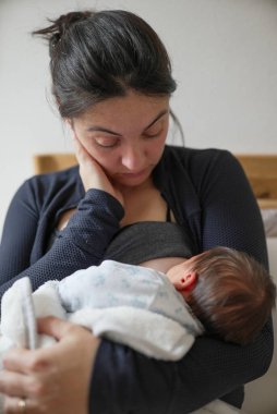 Bebekliğin ve ebeveynliğin ilk zorluklarının altını çizerek, bir ebeveyn tarafından nazikçe kucaklanarak ağlayan yeni doğan bir bebek. O hassas an, hayatın ilk haftalarının duygusal derinliğini ve kırılganlığını yakalar.