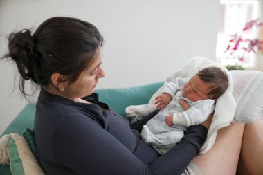 Anne ağlayan bebeğine bakıyor, ebeveynliğin ilk zorluklarını ve duygusal anlarını yakalıyor. Bu resim, anne ile çocuk arasındaki hassas ilgiyi ve derin bağı gösterir.