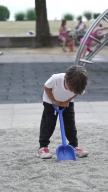 Oyun sahasında, Heyecanlı Genç Çocuk Oyuncak Küreği Havada Yükseğe Kaldırıyor Heyecan