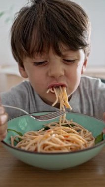 Küçük çocuk spagetti yerken heyecanlanıyor, yemek için eğlenceli ve lezzetli bir yol, çatal kullanarak hamur yuvarlıyor, gündüz mavi kase, İtalyan yemeği