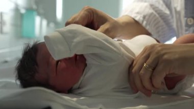 Yeni doğmuş bir bebek, hastanede şefkatli ellerle beyaz tulum giyer, doğumdan hemen sonra yeni doğanlara gösterilen hassas ve hassas ilgiyi gösterir.