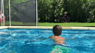 Çocuk yazın mavi suyla havuzda yüzüyor.
