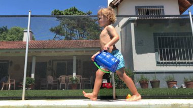 Toddler baby boy walking by the poolside, swimming pool setting at home