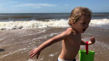 Infant toddler running at the beach with bucket filled with water playing