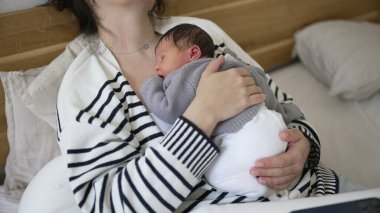 Anne, uyuyan yeni doğmuş bebeği göğsüne yakın tutuyor. Hayatının ilk günlerinde öğle uykusunda sevgiyle ve özenle kucaklıyor.