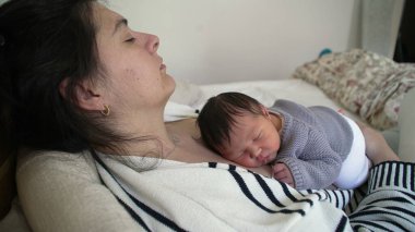 Yorgun bir anne, bebeğini kucağında tutarken annesinin göğsünde derin bir uykuda dinleniyor. İlk gün bebek ve ebeveyn arasında bir annelik bağı oluşuyor.