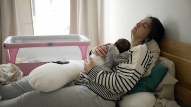 Yorgun bir anne, yeni doğmuş bir bebekle yatakta yatar, hayatının ilk günlerinde göğsünde uyur, anne öğleden sonra kestirir, anne bakımı yapar.