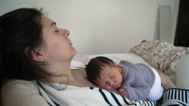 Yorgun bir anne, bebeğini kucağında tutarken annesinin göğsünde derin bir uykuda dinleniyor. İlk gün bebek ve ebeveyn arasında bir annelik bağı oluşuyor.