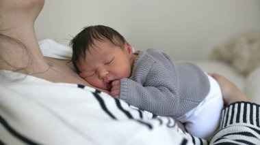 Yeni doğan bebek annesinin göğsünde dinleniyor. Yaşamın ilk günlerinde sevgi ve annelik bakımıyla sarılıp uyuyor.