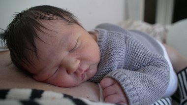 Yeni doğmuş bebek, hayatının ilk günlerinde annesinin göğsünde uyuyor. Huzurlu uykusunda uyuyan bebek.