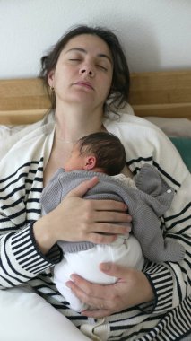 Öğleden Sonra Kestirme Sahnesi - Yorgun Anne ve Yenidoğan Bebek 'in İlk Günleri sırasında Yatakta Birlikte Uyuyor, dikey video. Bebek göğsünde tutuluyor.