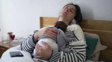 Yeni doğmuş bir bebekle hayatının ilk günlerinde göğsünde uyumaktan yorgun bir anne, yorgun bir anne yatakta uzanmış bebeği tutuyor ve ilk hafta dinlenmeye çalışıyor.