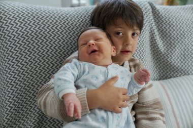 Küçük tatlı bir çocuk, kardeşini bir kanepede tutuyor. Kardeş ilişkilerinin masumiyetini ve hassasiyetini vurguluyor.