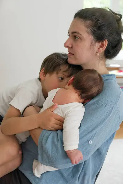 Stock image Mother with baby and young child, balancing care and attention between them, showcasing the tender moments of motherhood and the challenges of multitasking in a loving family setting