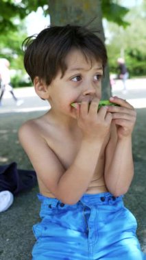 Çocuk bir dilim karpuzun tadını çıkarıyor, açık ve güneşli bir ortamda ferahlatıcı bir yaz meyvesi yemenin sevincini ve neşesini gösteriyor.
