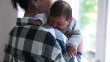 Yeni doğan bebek annesinin omzunda dinleniyor. Mutlu ve sakin görünüyor. Huzurlu bir bağ kurma anını vurguluyor.