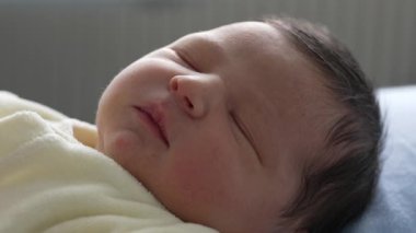 Yeni doğmuş bebek sakin bir ifadeyle uyuyor, yumuşak sarı bir battaniyeye sarılmış. Bebeğin dingin yüzüne odaklanarak, bebekliğin sükunetini ve saflığını vurguluyor.