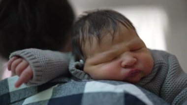 Anne, huzurlu, güneşli bir odada bebeğini nazikçe omzunda tutuyor. Bebek mışıl mışıl uyuyor, anne ve çocuk arasındaki derin sevgiyi ve şefkati gösteriyor.