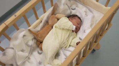 Yeni doğan bebek sarı tulumlu bir bebek hastane koridorunda taşınıyor, doğumdan sonraki ilk haftayı gösteriyor, aile, ebeveynlik ve sağlık hizmetleri için mükemmel.