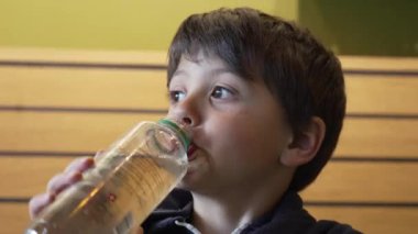 Şişeden buzlu çay içen genç çocuk, bir günlük düzende serinletici ve sağlıklı alışkanlıklara odaklanmış bir şekilde kapalı mekanda yakalandı.